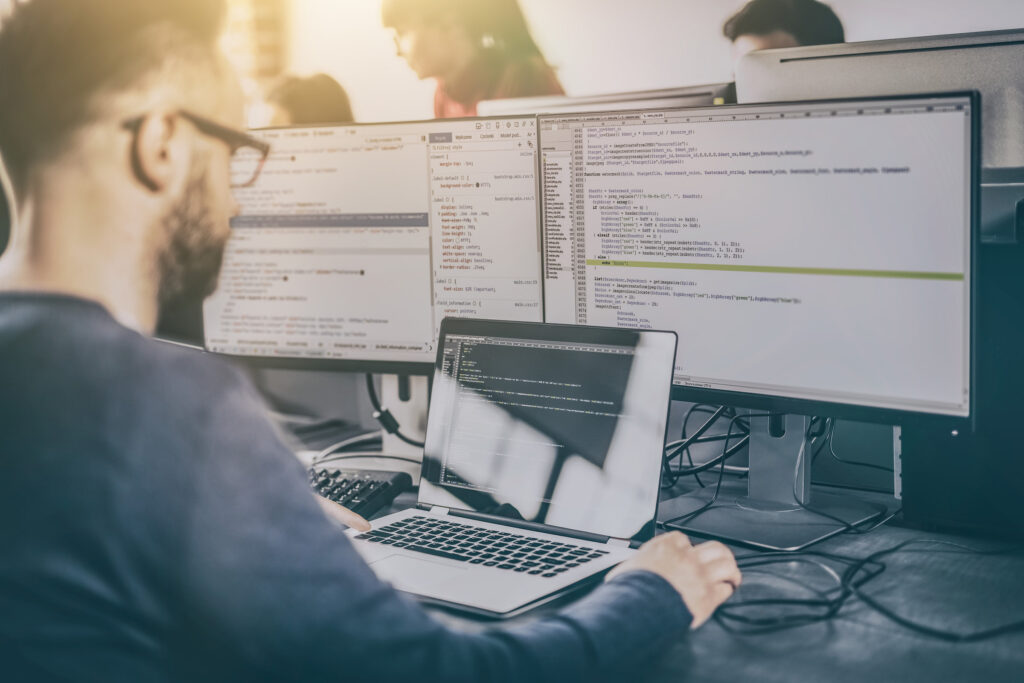 man writing code with HP laptop and dual monitors