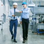 two men in manufacturing industrial plant reviewing laptop