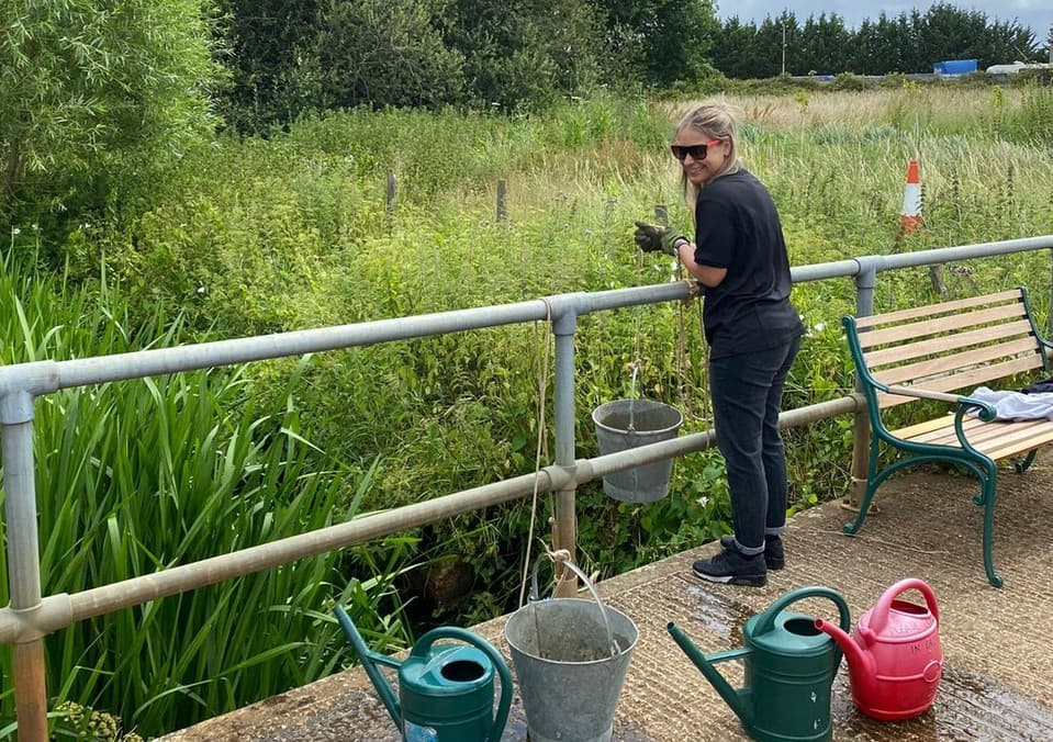 Toshiba volunteer gathers river water in a bucket at Holme Farm