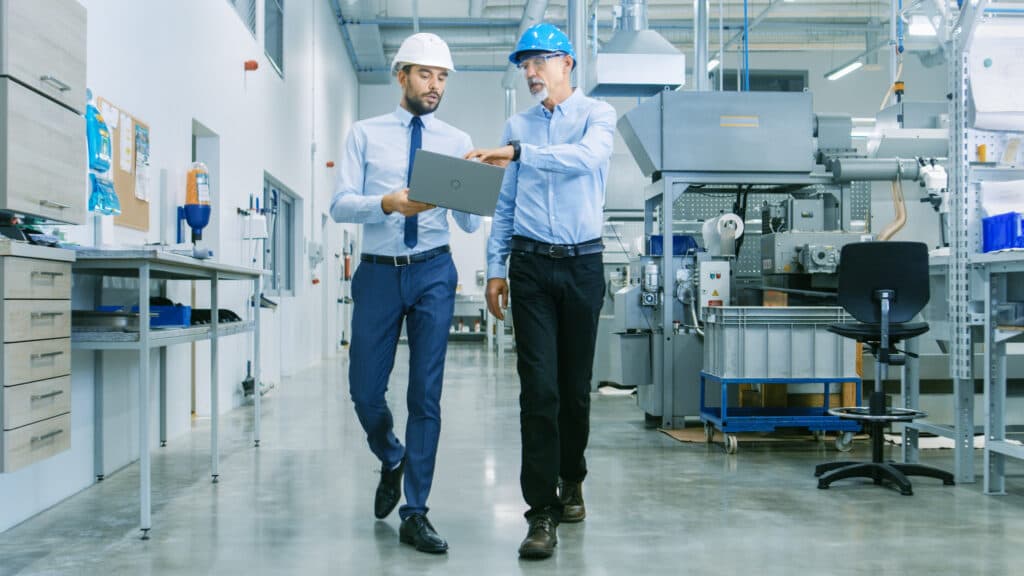 two men in manufacturing industrial plant reviewing laptop
