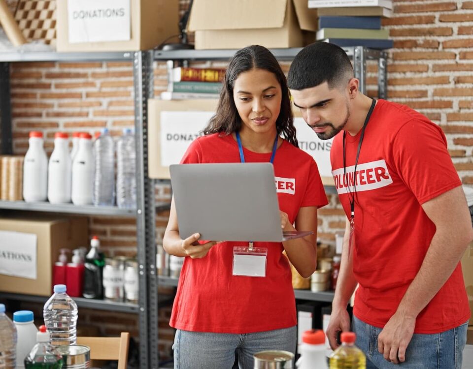 man and woman charity volunteers wearing red and taking inventory with a laptop