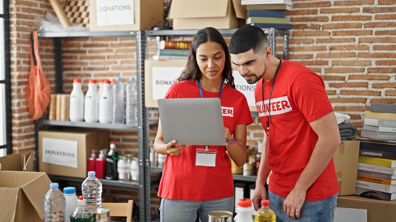 man and woman charity volunteers wearing red and taking inventory with a laptop