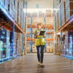 yellow vest warehouse worker woman taking inventory with laptop